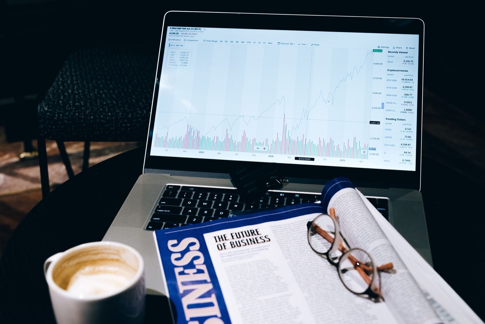 A market chart on a laptop beside a business magazine