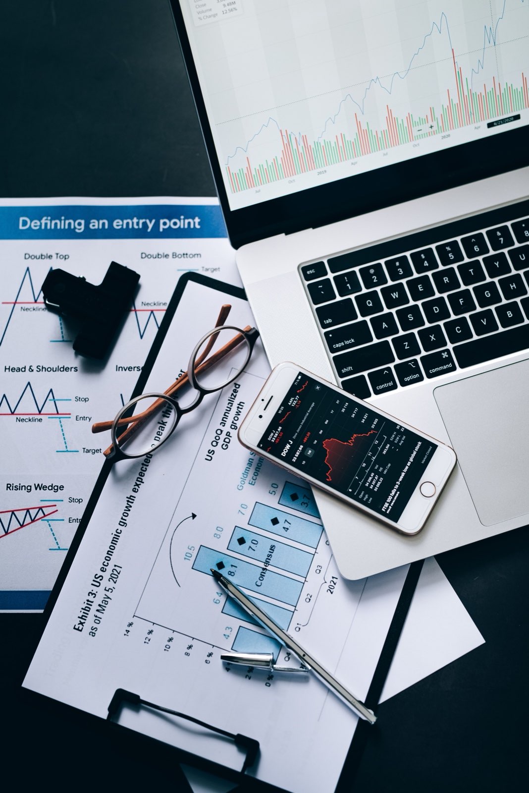 Market charts, reading glasses and a phone on a desk